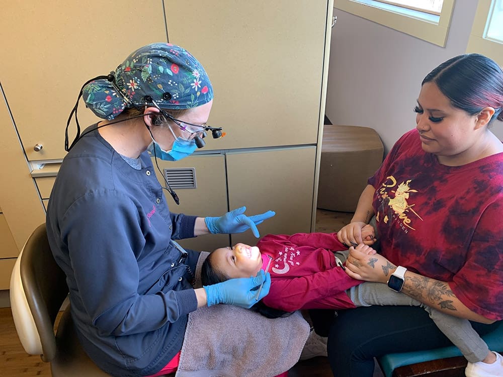 Female dentist examining the teech of a small kid while the mother is holding his hands. Pediatric Dentistry for kids with special needs