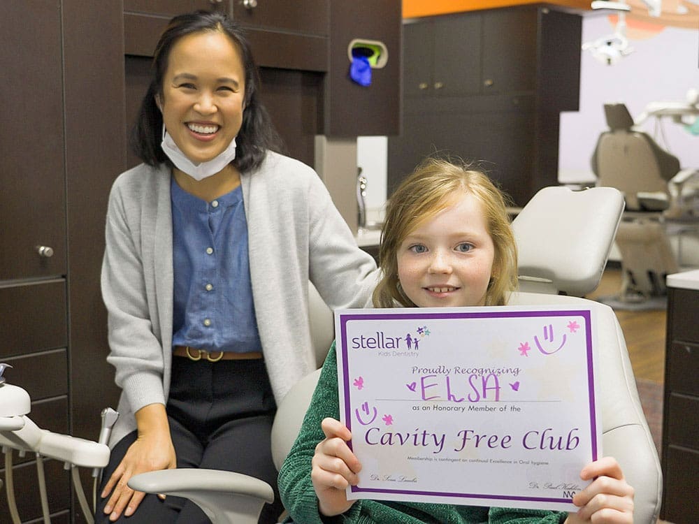 Dentist and Girl posing for a picture, girl holding a "Cavity free club" certificate Stellar pediatric dentist - Cavity free club.
